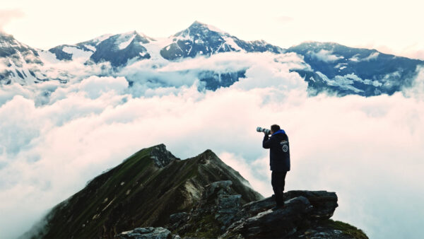 Eine Person fotografiert auf einem Berggipfel vor einem Wolkenmeer.